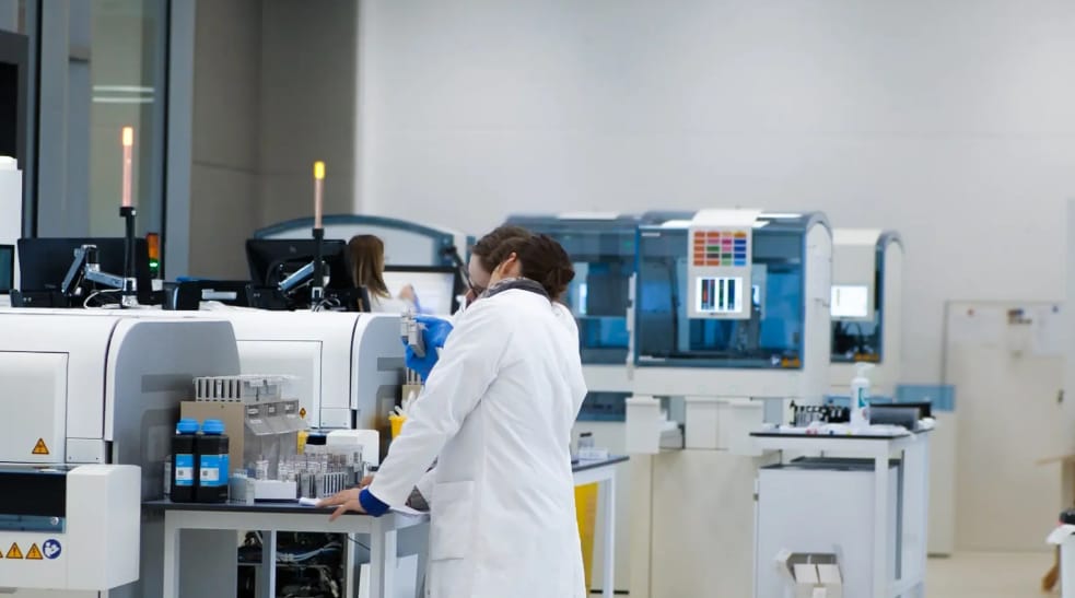 Technicienne en blouse blanche devant les automates d'analyse du laboratoire Lims